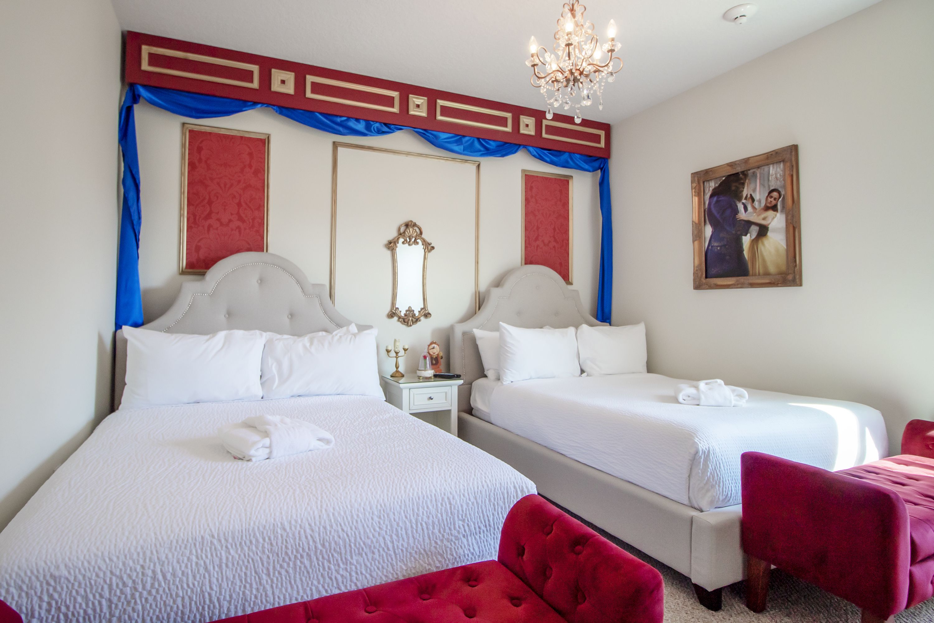 Ein Hotelzimmer mit zwei Betten, einer Kandelaber, einem Gemälde und roten Polstersesseln.