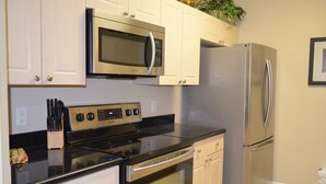 Una cocina con electrodomésticos de acero inoxidable, incluyendo microondas, horno y refrigerador, con gabinetes blancos y encimera negra.