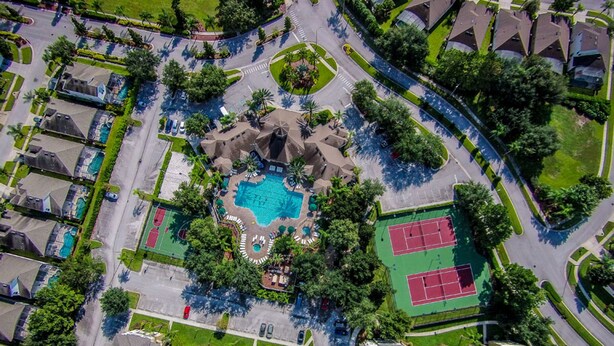 Vista aérea de una zona residencial con piscina central, canchas de tenis y un parque arbolado.