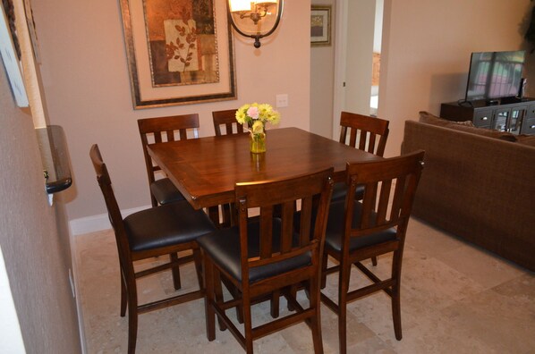A dining area with a wooden table and chairs, a vase with flowers, and a television on a cabinet.