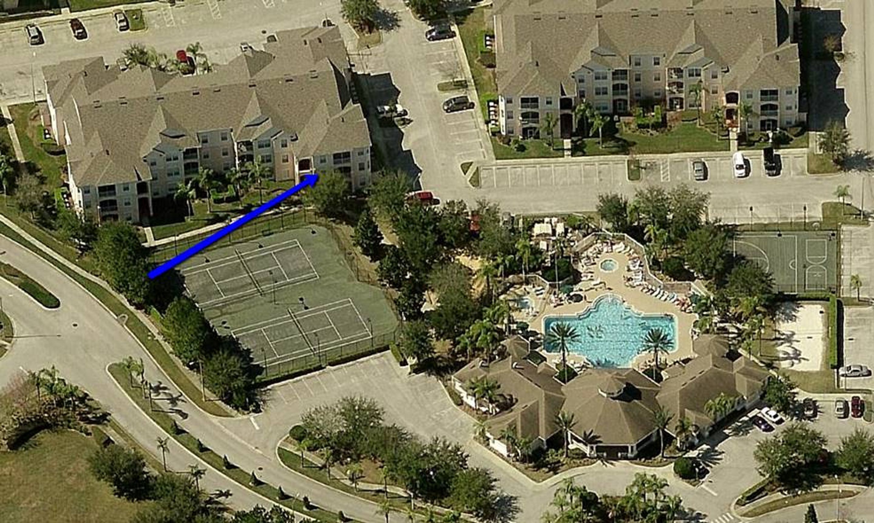 An aerial view of a residential area with multiple two-story houses, a tennis court, and a swimming pool complex.