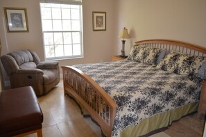 A bedroom with a bed, a chair, a nightstand, a lamp, and two framed pictures on the wall. - Windsor Palms 2303 - 203 (Kissimmee)