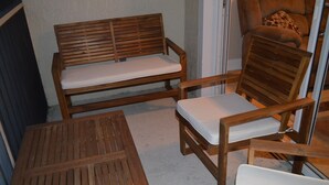 Un banco y una silla de madera con cojines blancos en una habitación con piso de concreto.