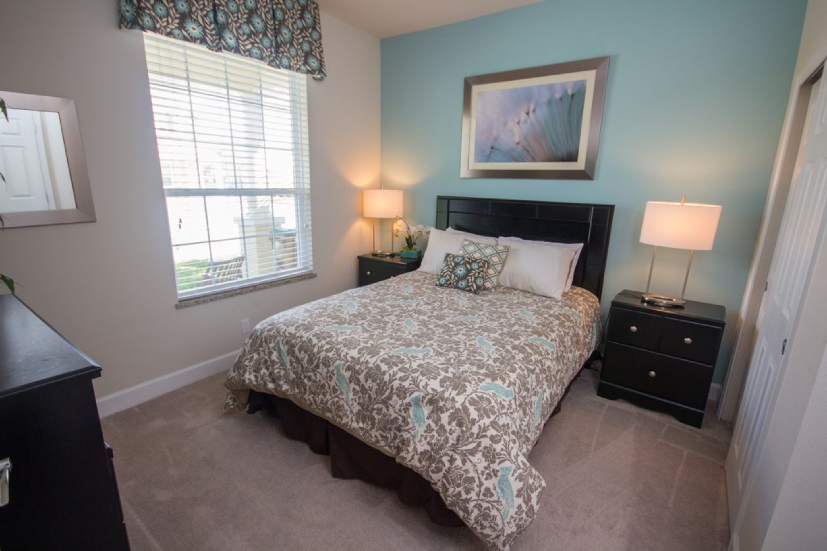 A bedroom with a bed, two bedside tables, a window with blinds, a painting on the wall, and a dresser.