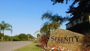 Een stenen bord met de tekst 'Serenity Townhomes', omringd door gras en bloemen.