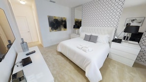 A hotel room with a large bed, white bedding, a bedside table with a lamp, and a wall with a geometric pattern.