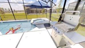 A swimming pool with a hot tub, a barbecue grill, and a large umbrella.