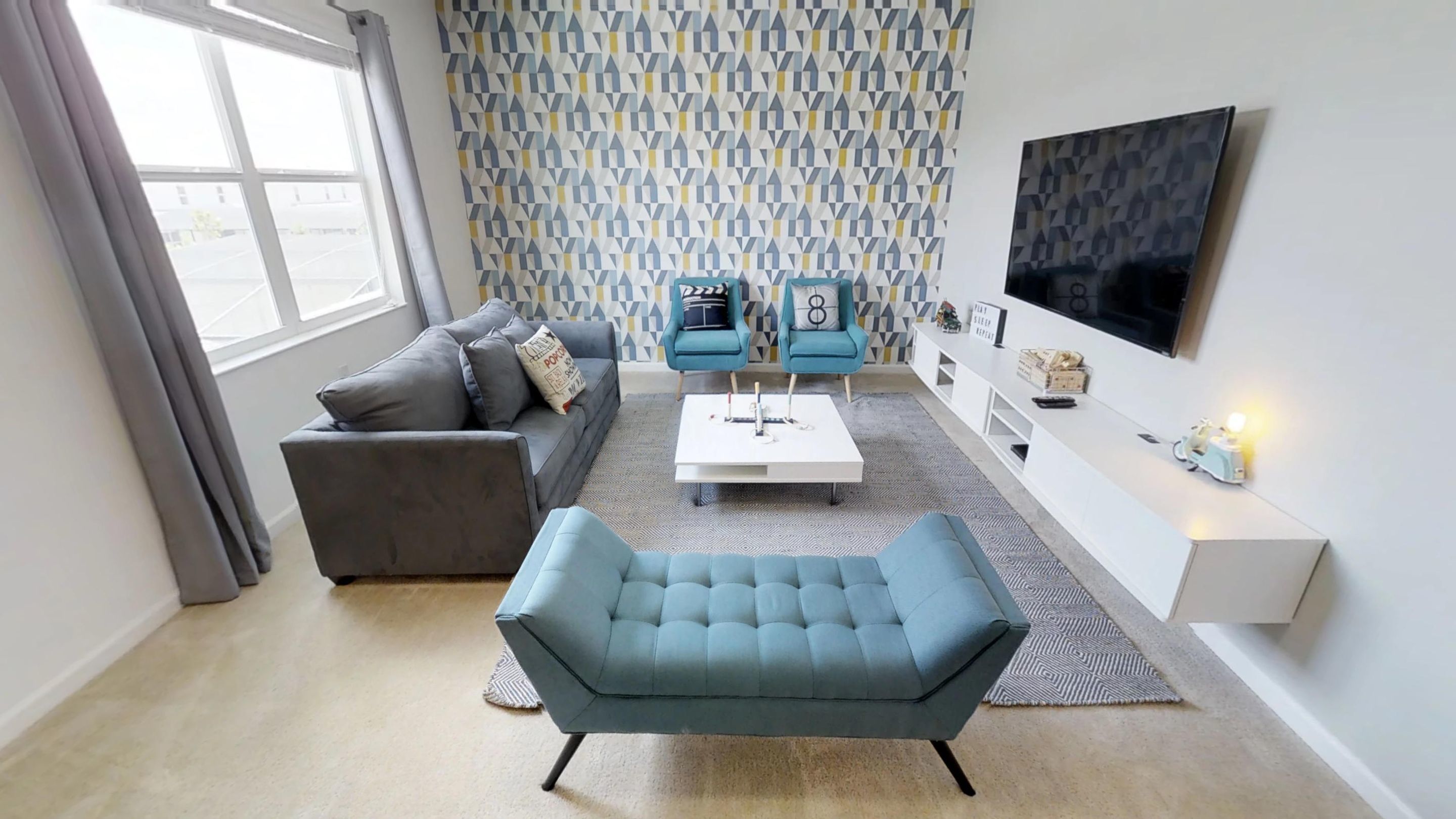 Ein modernes Wohnzimmer mit einem grauen Sofa, einem blauen Sessel, einem weißen Couchtisch und raumhoher Tapete mit Muster.