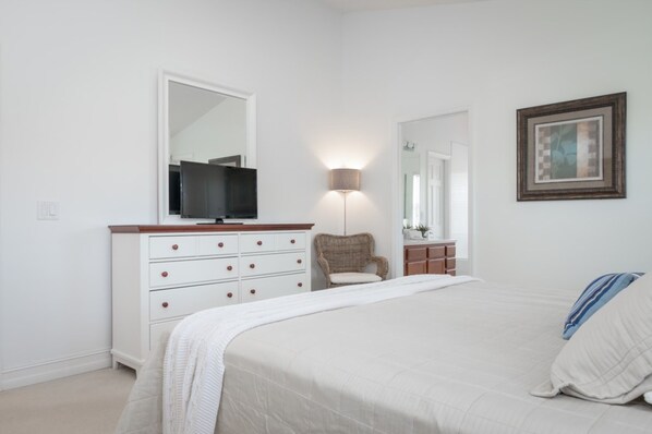 A bedroom with a bed, dresser, chair, and a television on a dresser.