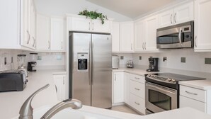 A modern kitchen with white cabinetry, stainless steel appliances, a built-in water dispenser, and a coffee maker. - Indian Creek 8115 (Kissimmee)