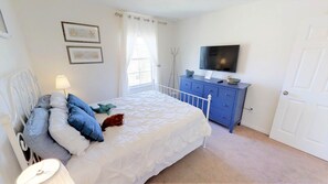 Quarto com cama, penteadeira, televisão e quadros nas paredes.