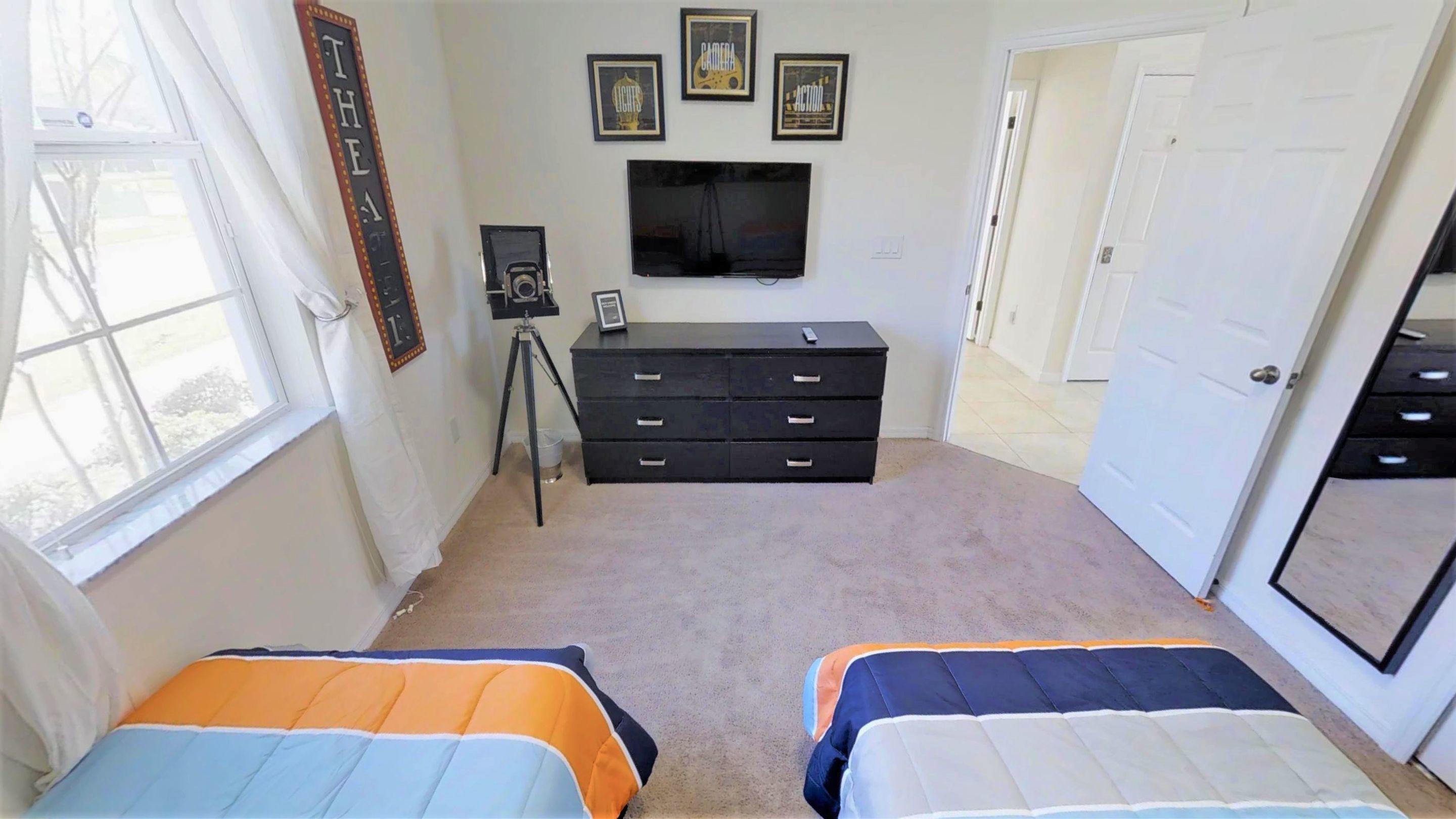 A bedroom with two beds, a dresser, a television, and framed pictures on the wall.