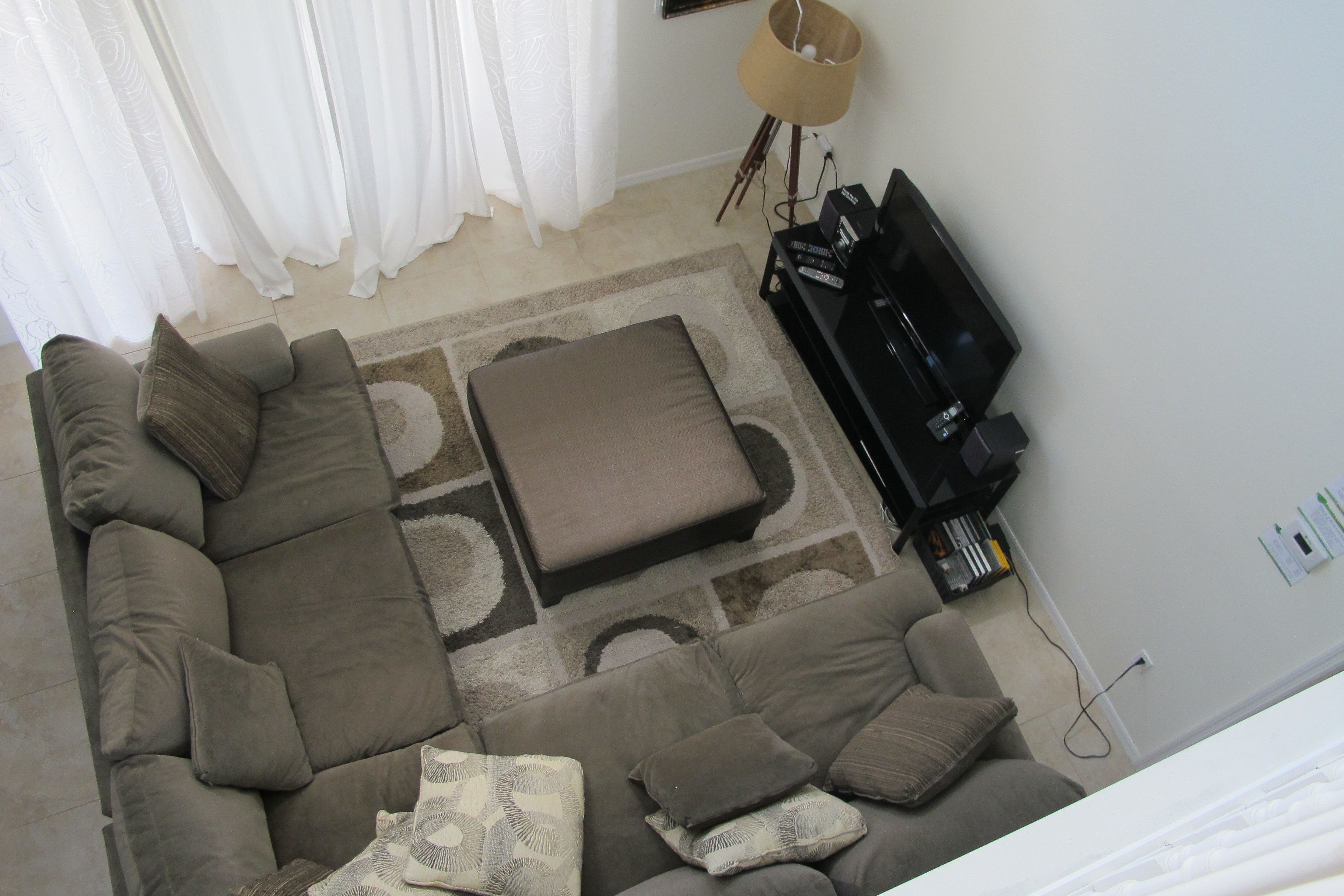 A living room with a sectional sofa, ottoman, and a flat-screen TV on a stand.