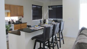 Een moderne keuken met houten kastjes, een eethoek met een lange tafel en stoelen, en een woonkamer met een bank.
