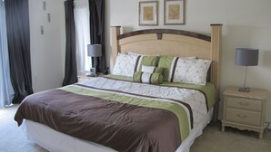 Een net opgemaakt bed met een bruin-groene sprei, een nachtkastje met een lamp, en twee ingelijste foto's aan de muur.