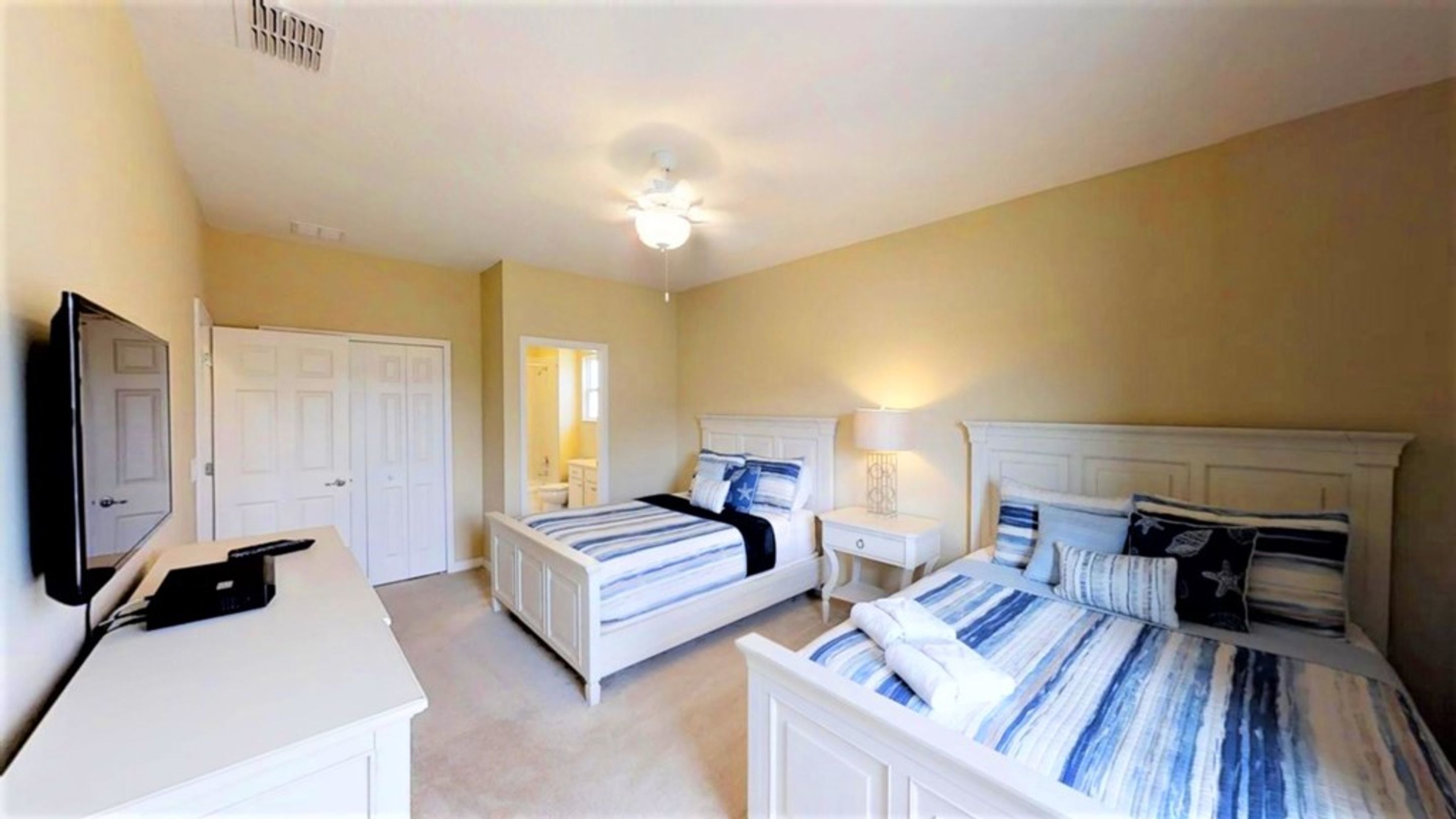 A hotel room with two beds, a desk, a TV, and a ceiling fan.
