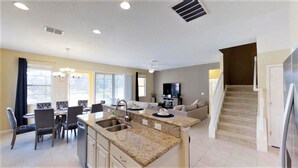 A modern kitchen with granite countertops, a dining area with chairs, a sofa, and a TV in the living room. - Golden Palms Vacation Resort 4439 (Kissimmee)