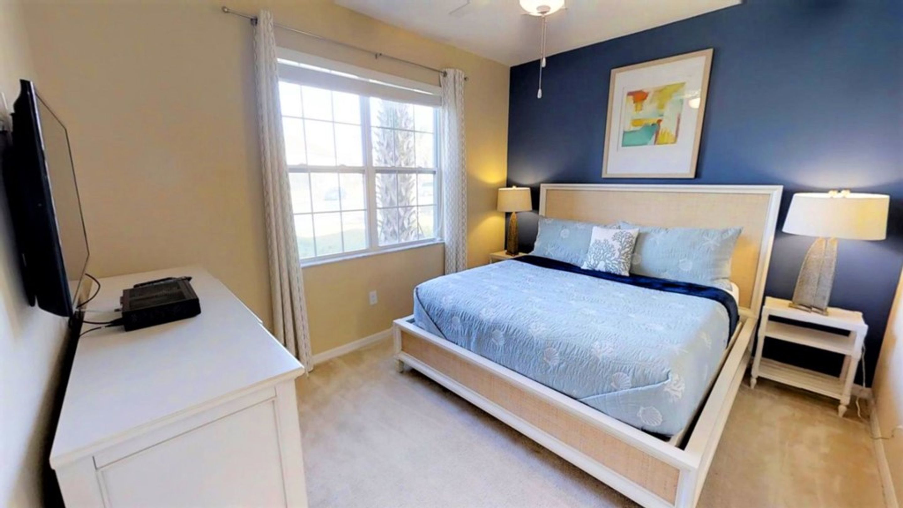 A bedroom with a bed, bedside tables, a TV, and a window.