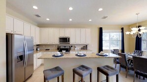 A modern kitchen with white cabinets, stainless steel appliances, and a central island with stools. - Golden Palms Vacation Resort 4439 (Kissimmee)