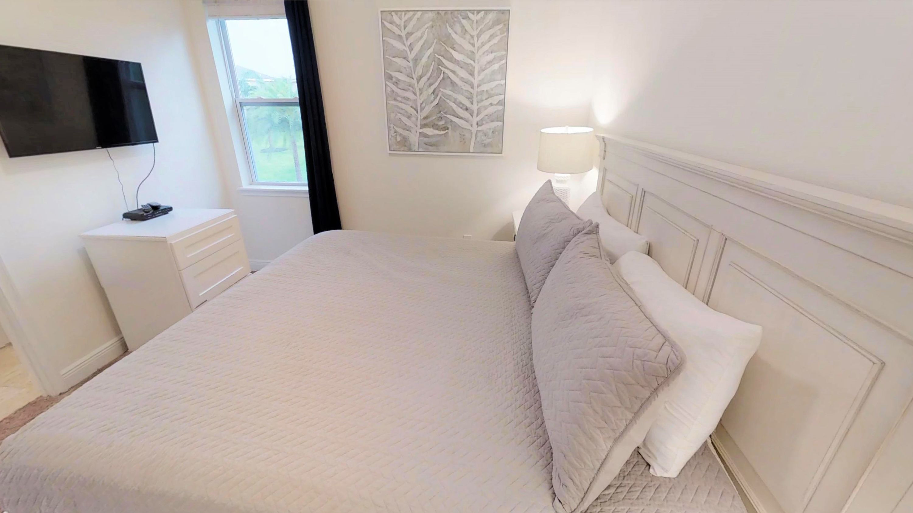 A neatly arranged bedroom with a bed, bedside table, lamp, and artwork on the wall.