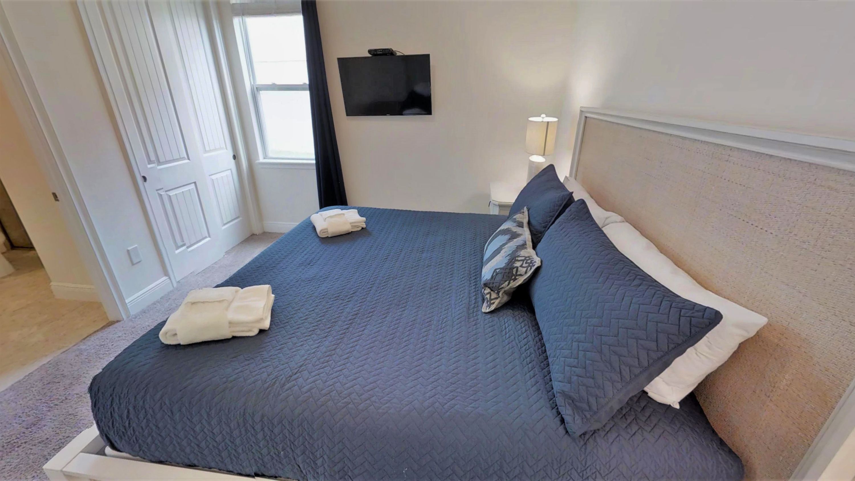 Ein ordentlich bezogenes Bett mit einer blauen Decke, zwei Kissen und gefalteten Handtüchern.