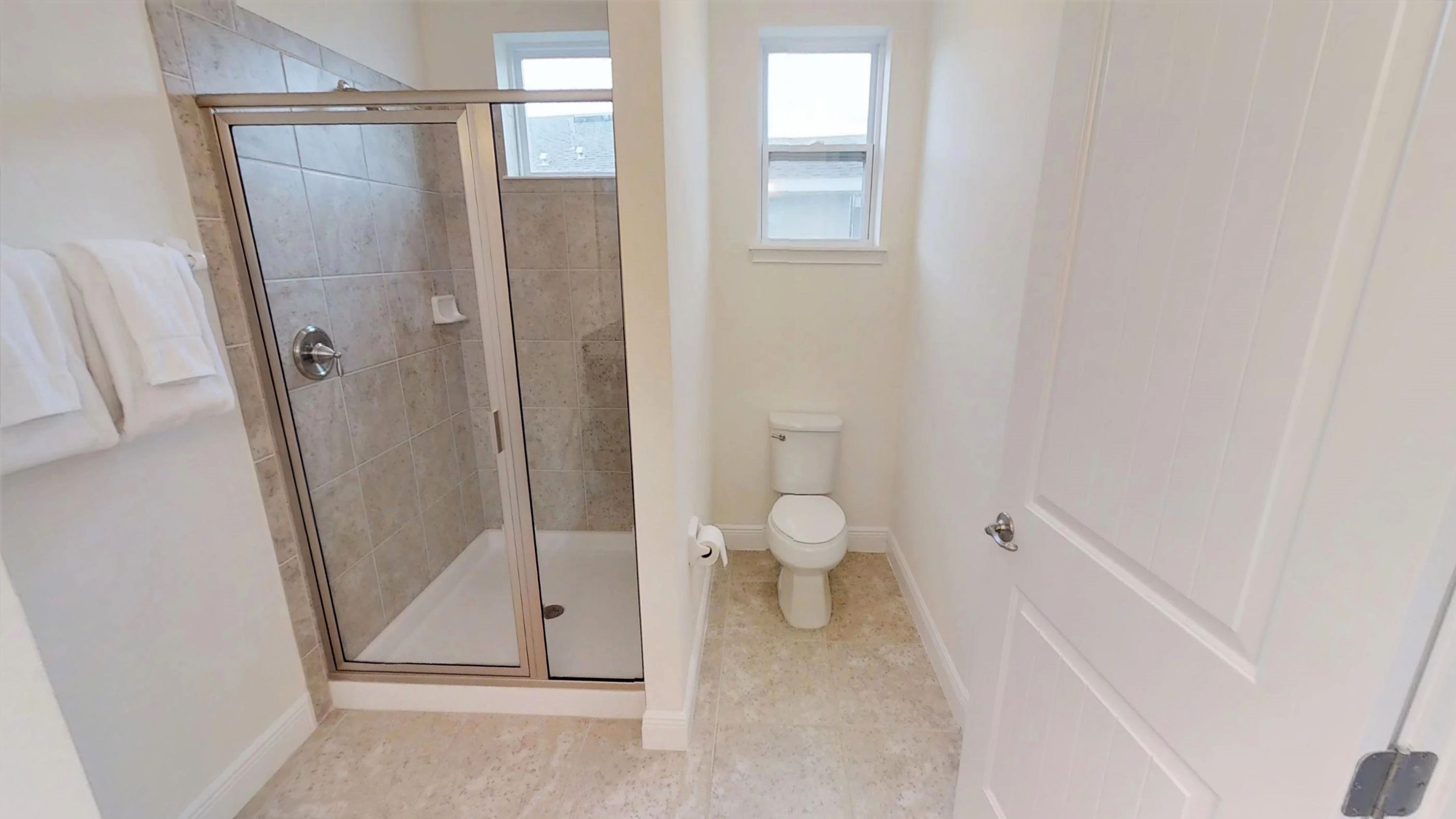 A bathroom with a glass shower enclosure, a toilet, and a window providing natural light.