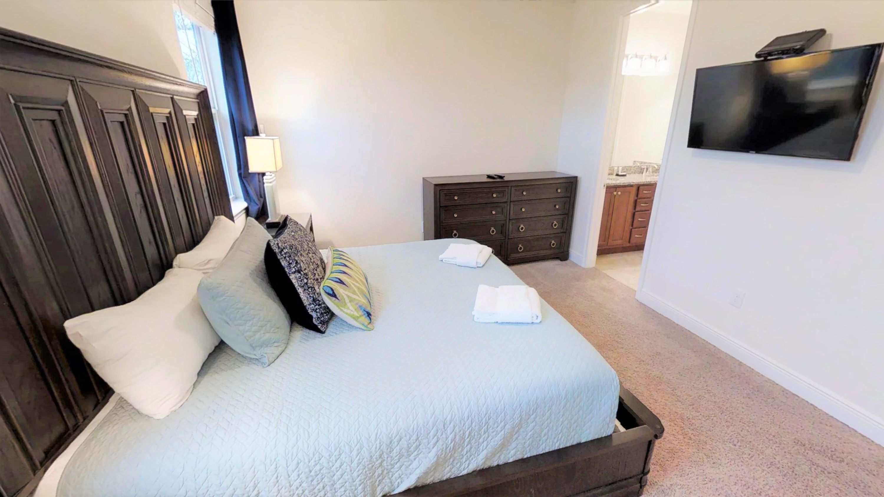 A bedroom with a bed, pillows, a dresser, and a TV on the wall.