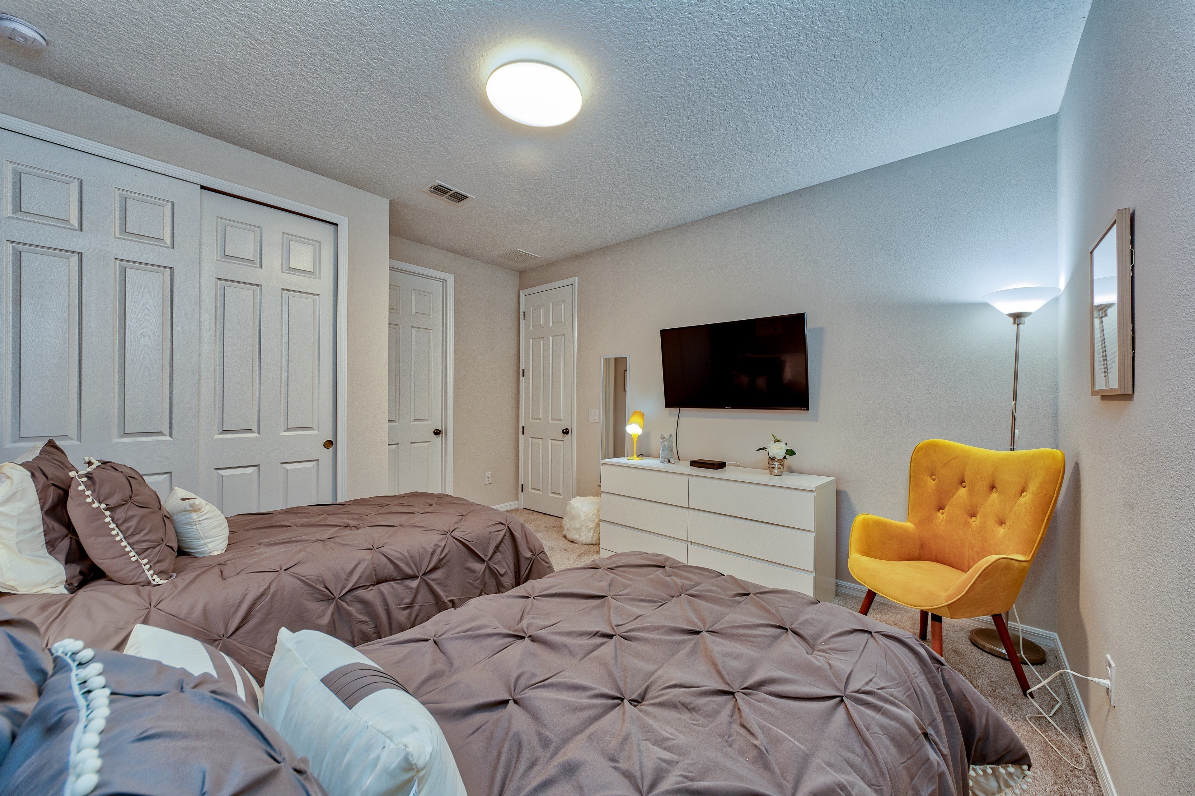 A bedroom with two beds, a dresser, a chair, and a TV on the wall.