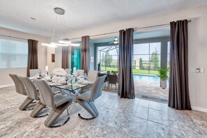 A dining area with a glass table, modern chairs, and a view of a swimming pool. - Solara Resort 9047 (Kissimmee)