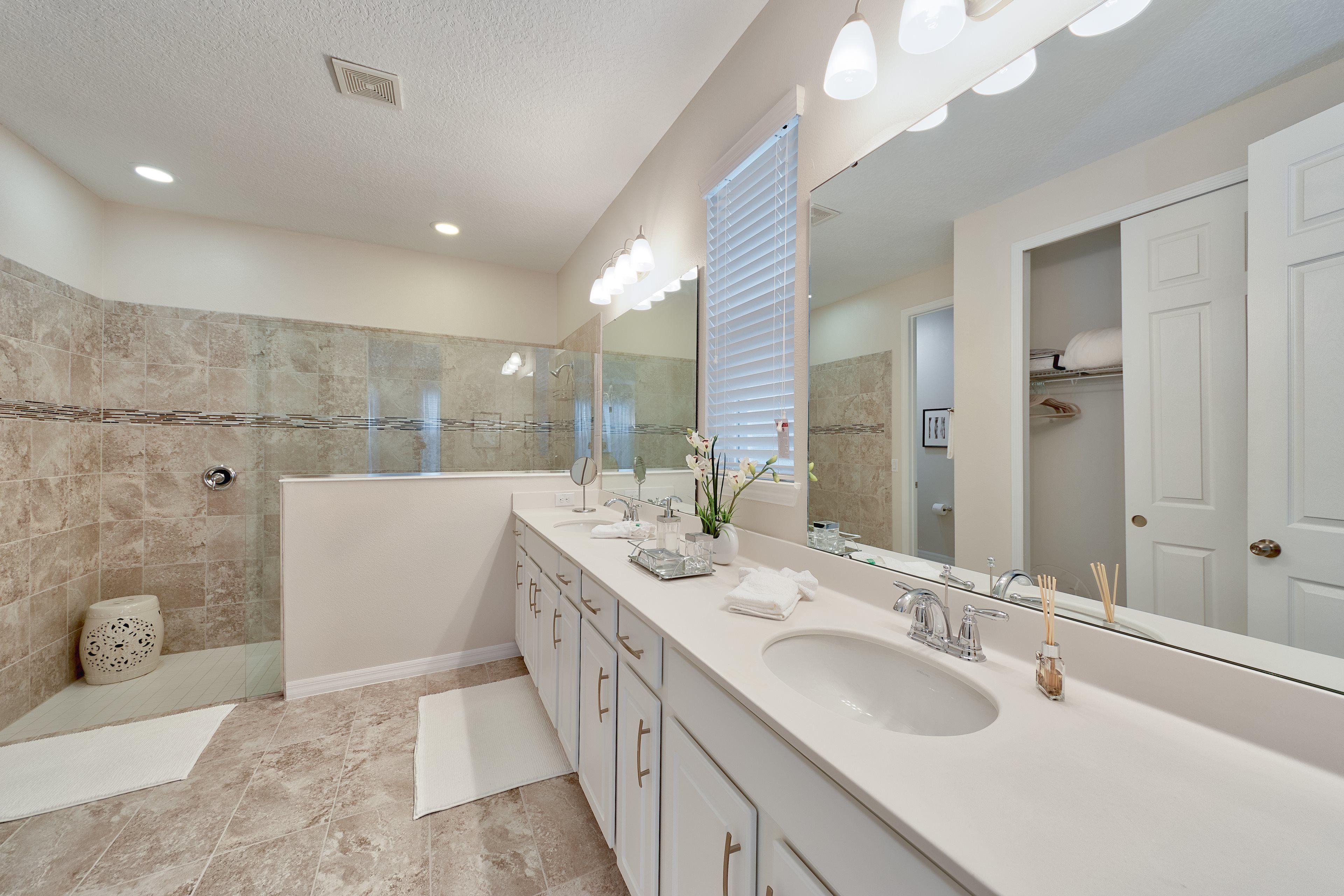 A modern bathroom with a large mirror, two sinks, and a walk-in shower.