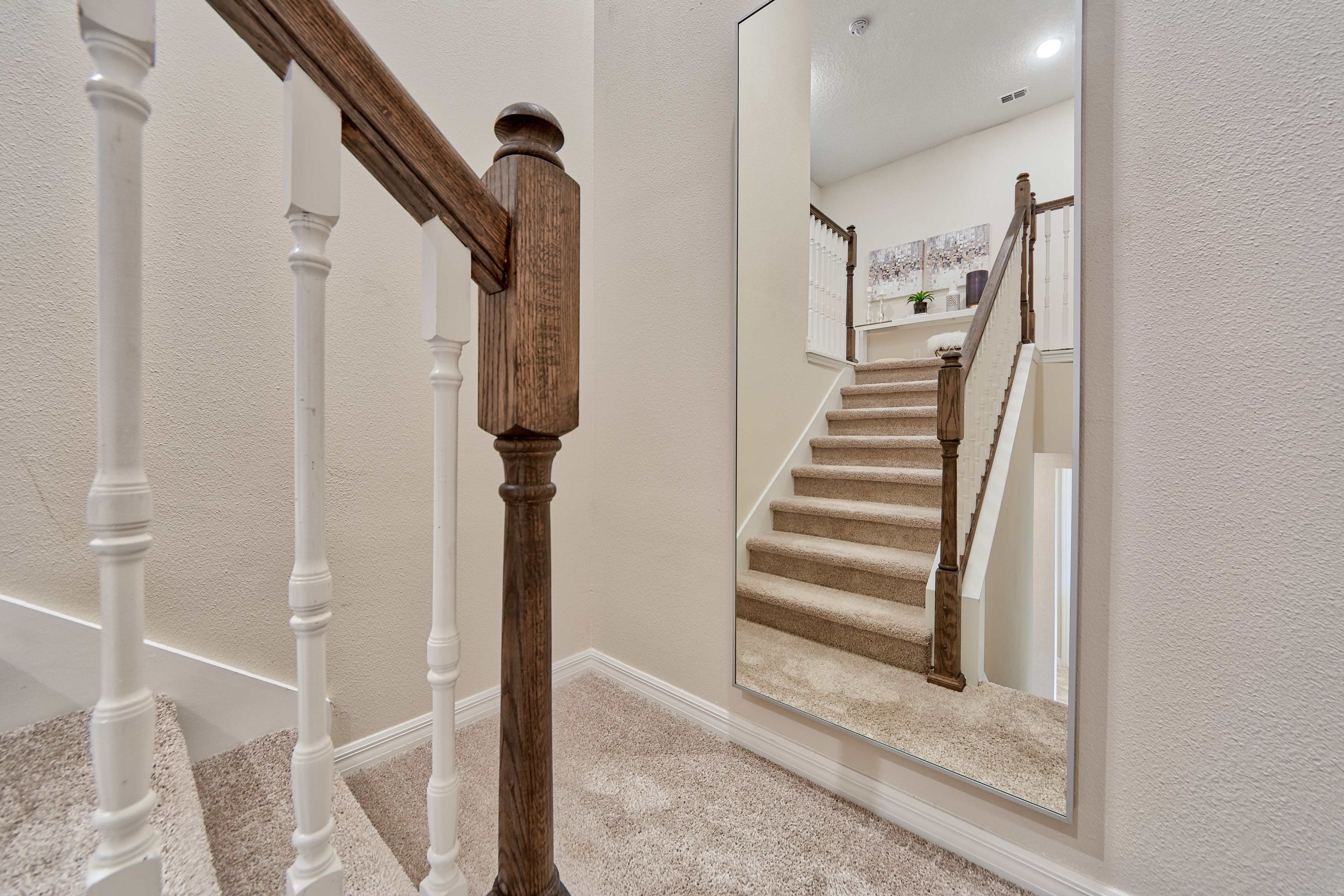 A staircase with white balusters and wooden handrails, carpeted steps, and a large mirror reflecting the staircase.