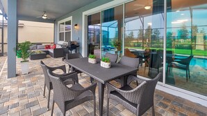 Ein überdachter Patio-Bereich mit Esstisch und Stühlen, einem Grill und Kübelpflanzen.