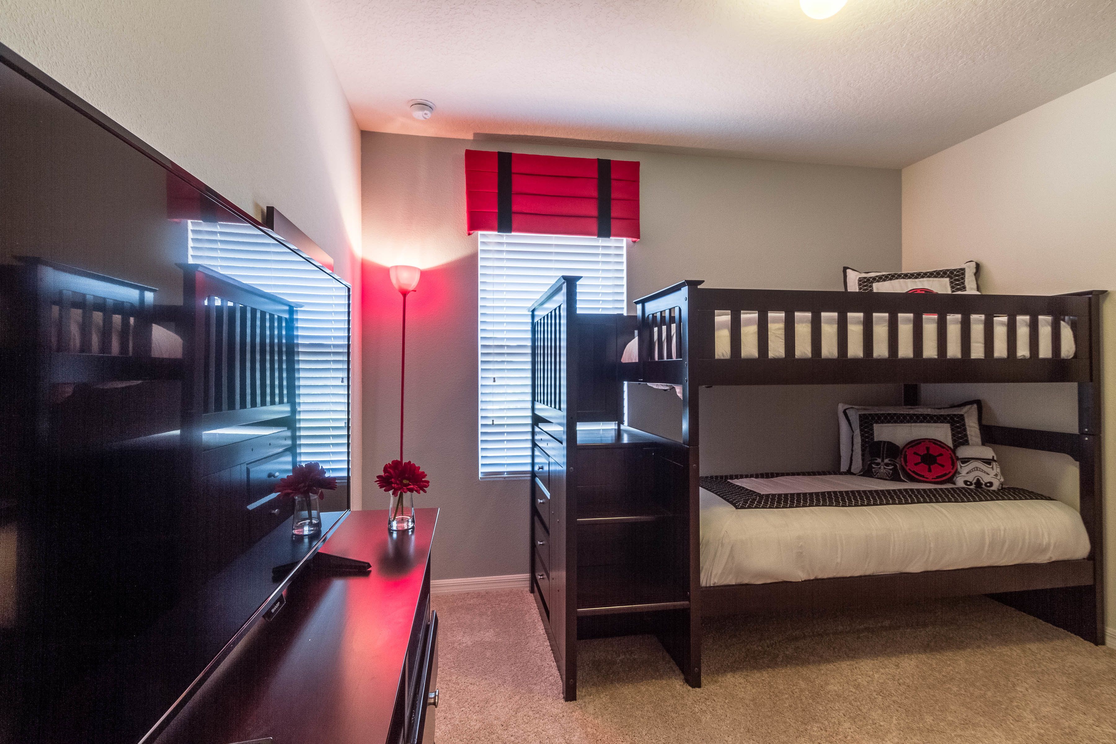 A bedroom with a bunk bed, a desk with a lamp, and a window with blinds.