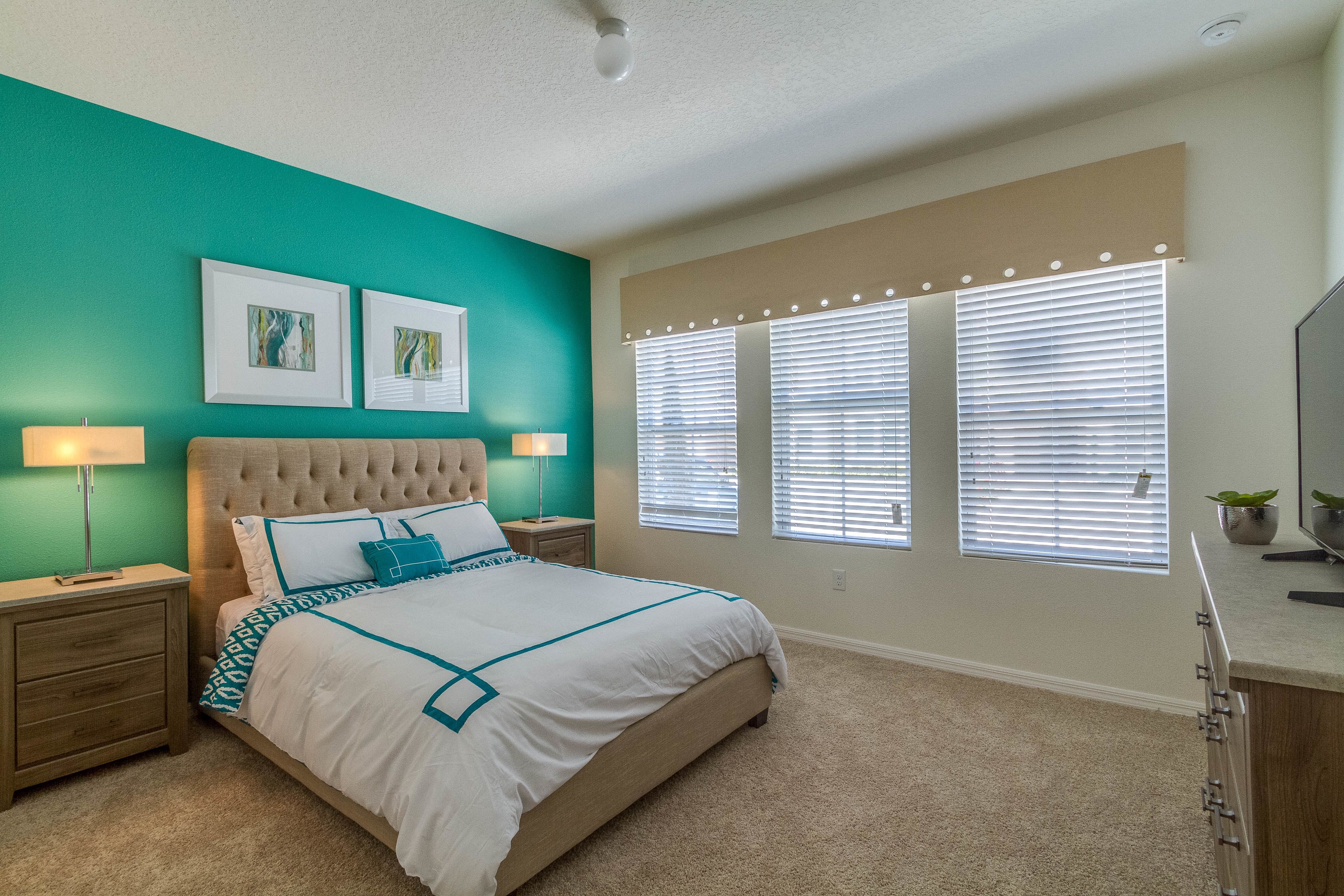 A bedroom with a large bed, two bedside tables with lamps, a ceiling fan, and a window with blinds.