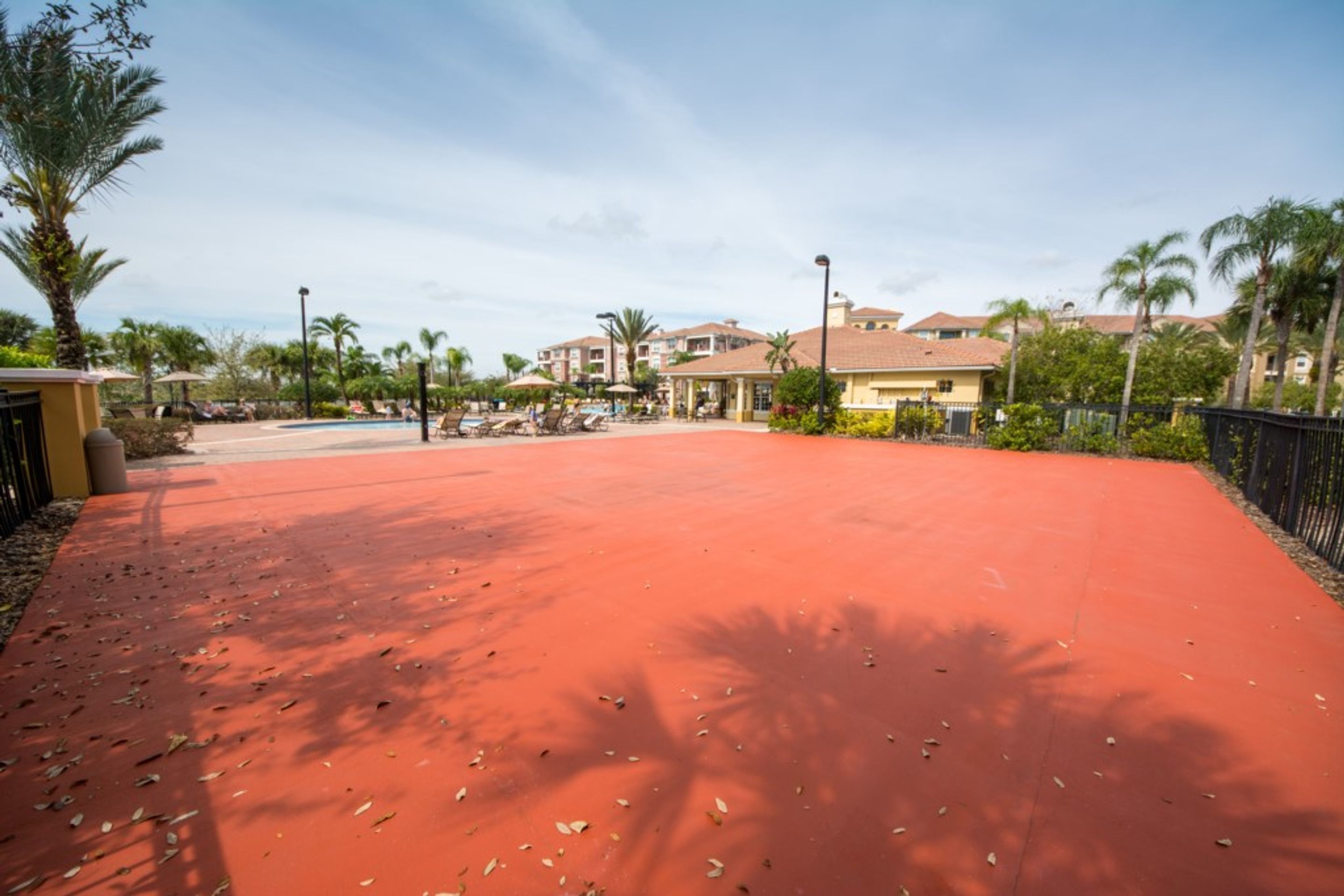 Ein roter, mit Ziegeln belegter Weg führt zu einem Poolbereich mit Palmen und einem Gebäude im Hintergrund.