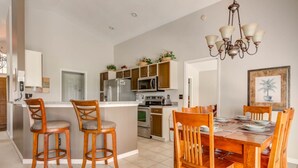 A kitchen with a central island, wooden chairs, a dining table set for six, and a chandelier.