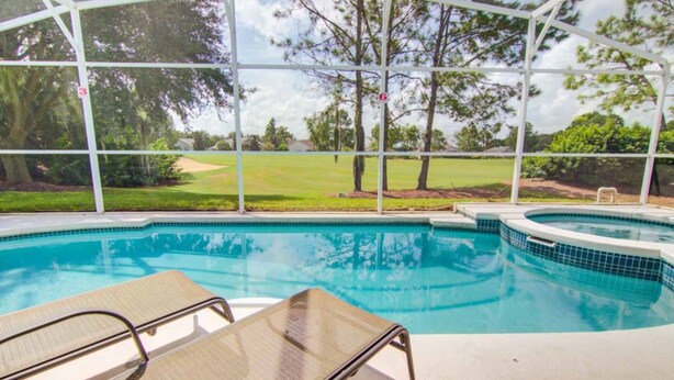 A pool area with a covered section, lounge chairs, and a view of a golf course.