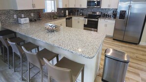 Eine moderne Küche mit weißen Schränken, Granit Arbeitsplatten, Edelstahlgeräten und Barhocker.
