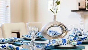 A dining table set with blue floral tablecloths, silverware, and clear glassware. - Veranda Palms 2505 (Kissimmee)