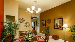 A dining room with a round table set for four, surrounded by chairs, a chandelier, and wall-mounted artwork. - Windsor Hills 7718 (Kissimmee)