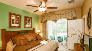 A bedroom with a bed, a ceiling fan, a door leading to a balcony, and framed pictures on the wall. - Windsor Hills 7718 (Kissimmee)