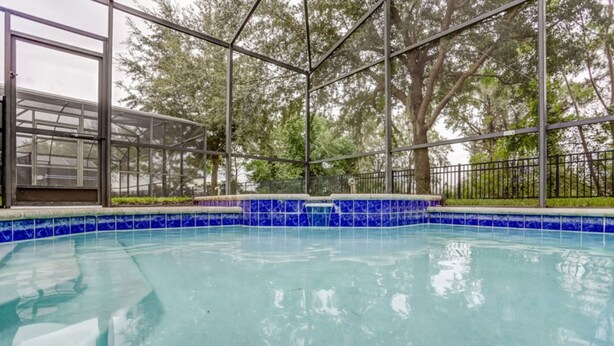 A swimming pool with blue tiles, surrounded by metal railings and trees. - Windsor Hills 7718 (Kissimmee)