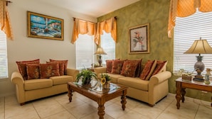 A living room with two beige sofas, a glass coffee table, and a painting on the wall. - Watersong 457 (Davenport)