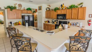 A spacious kitchen with wooden cabinets, a central island, and bar stools. - Watersong 457 (Davenport)
