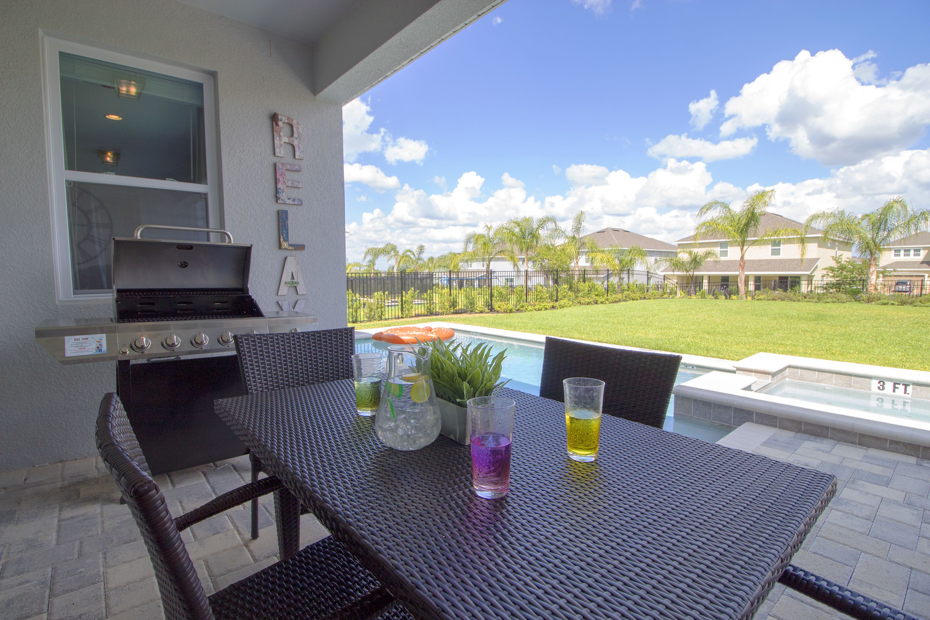 Eine Terrasse im Freien mit Grill, Sitzgelegenheit und Blick auf ein Schwimmbad und Häuser.