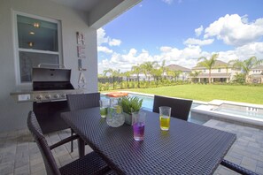 An outdoor patio with a grill, seating, and a view of a swimming pool and houses. - Encore Resort at Reunion 7711 (Kissimmee)