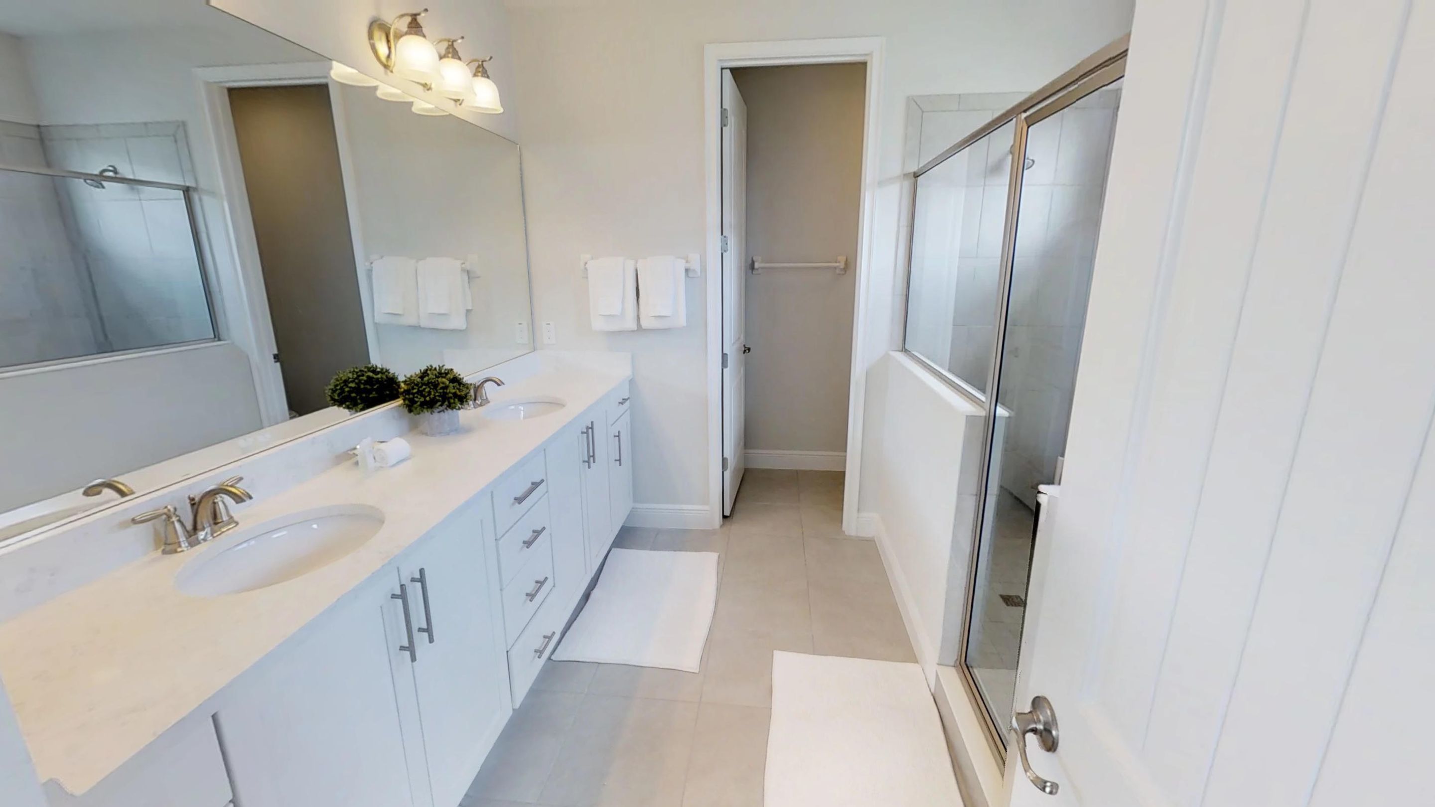 Een moderne badkamer met een grote spiegel, twee wastafels, een douche en een inloopkast.