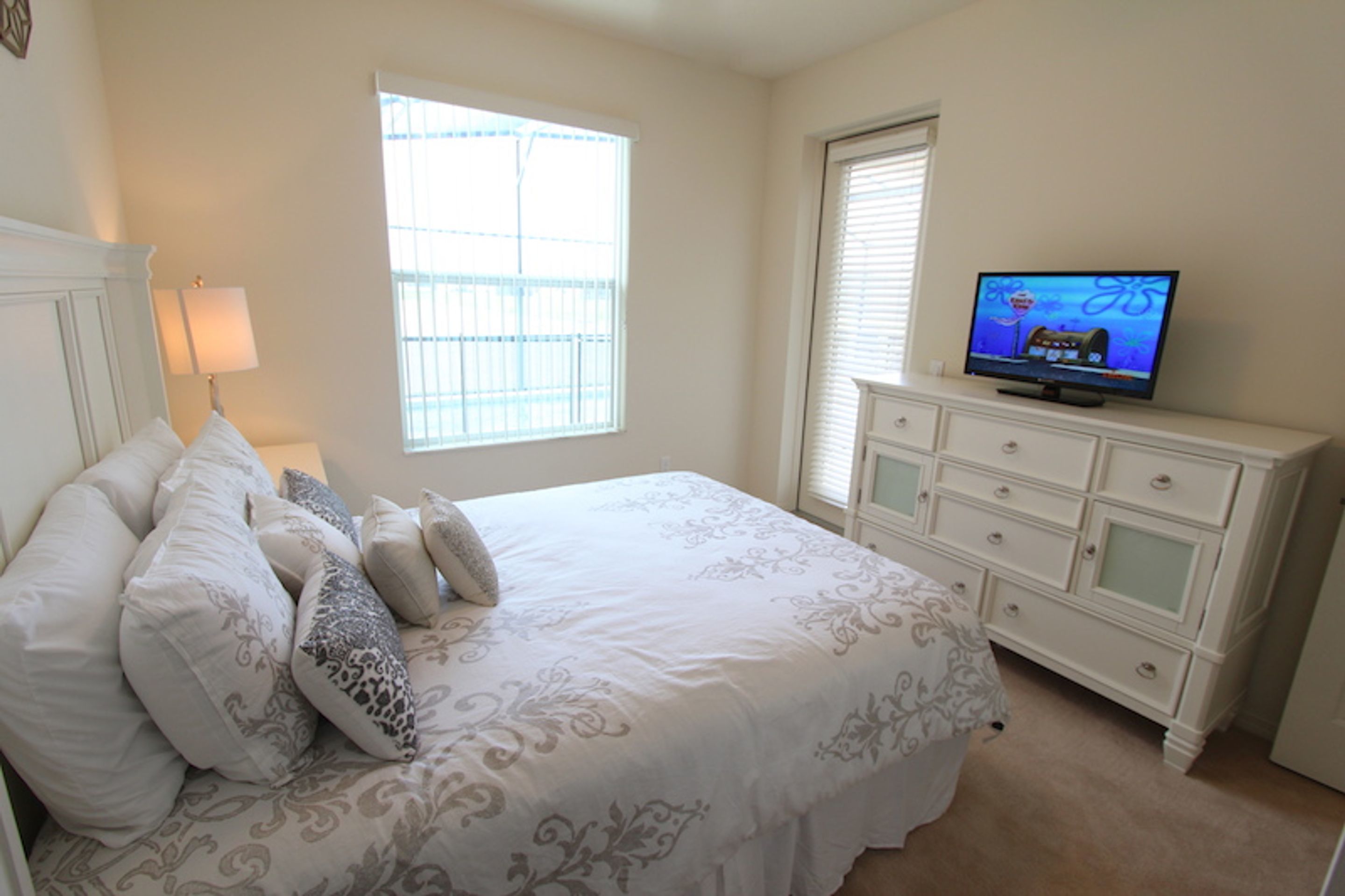 Quarto com cama, televisão em uma cômoda e janela com persianas.