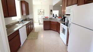 A modern kitchen with granite countertops, wooden cabinets, a built-in oven, and a white refrigerator. - Crystal Cove 1014 (Kissimmee)