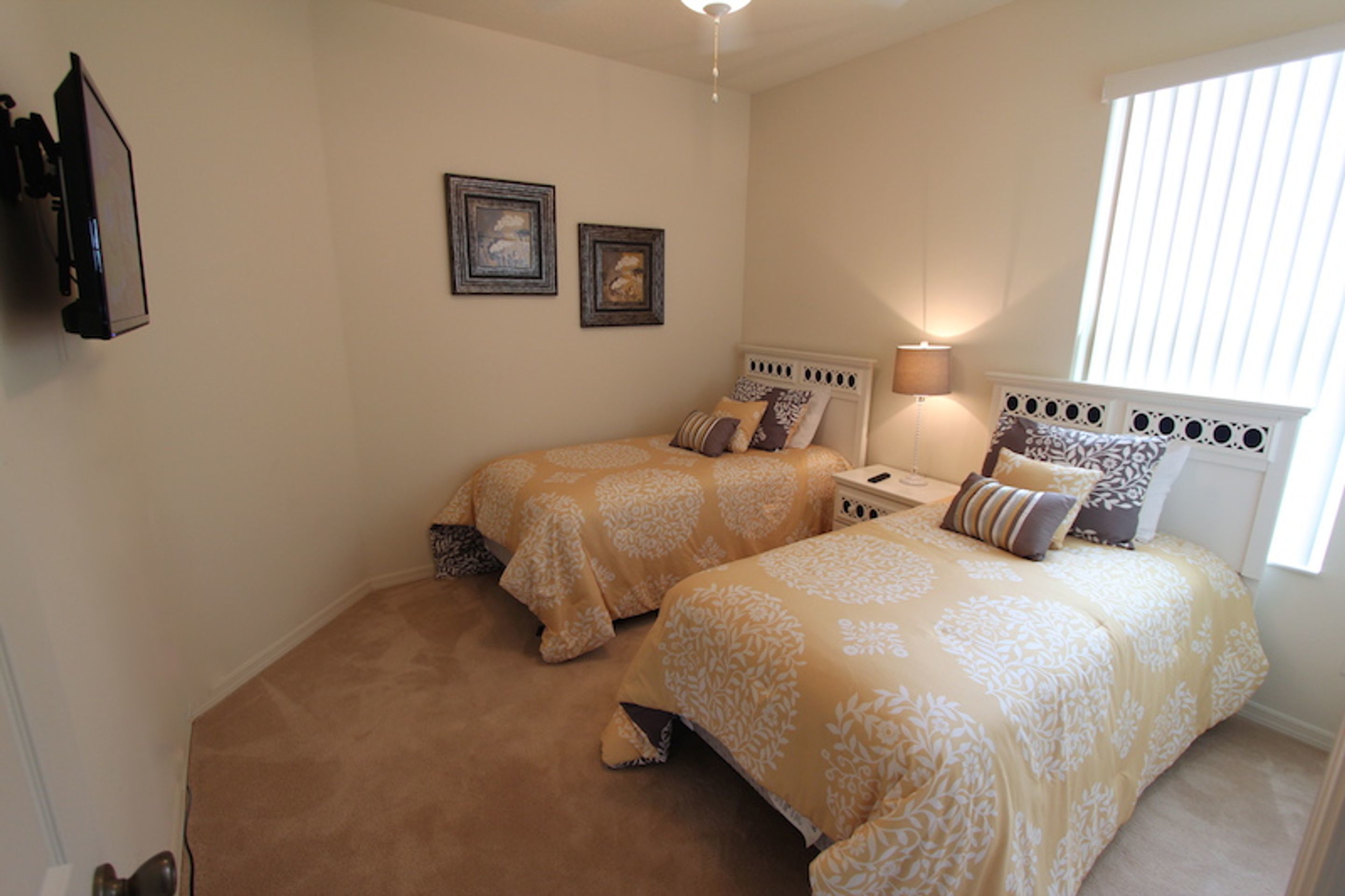A bedroom with two beds, a nightstand, a lamp, and a window with blinds.